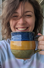 A smiling woman with brown hair holds a large, striped ceramic mug close to her face.